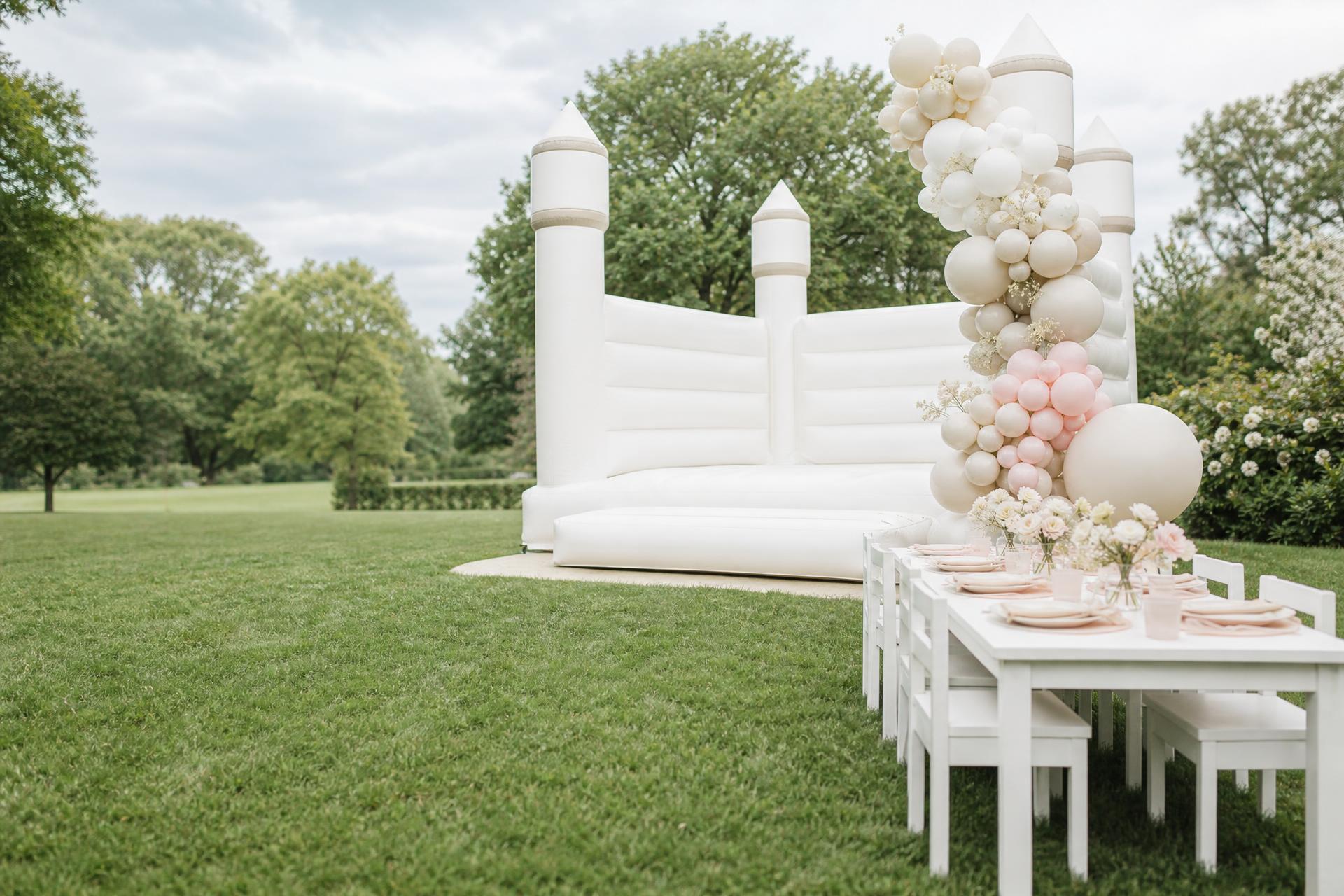 Weiße Premium Hüpfburg mit pastellfarbener Ballondekoration bei einem Kindergeburtstag im Garten